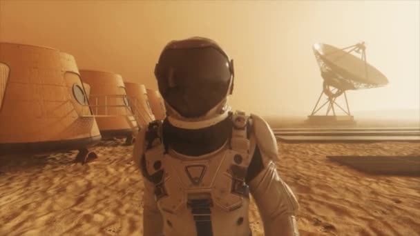 Astronauta en el planeta Marte, haciendo un desvío alrededor de su base. Astronauta caminando por la base. Pequeña tormenta de polvo. La antena parabólica envía datos al suelo. Animación 3D realista — Vídeo de stock