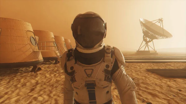 Mars gezegenindeki astronot, üssünün etrafından dolanıyor. Astronot üs boyunca yürüyor. Küçük bir toz fırtınası. Uydu anten yere veri gönderiyor. 3B illüstrasyon