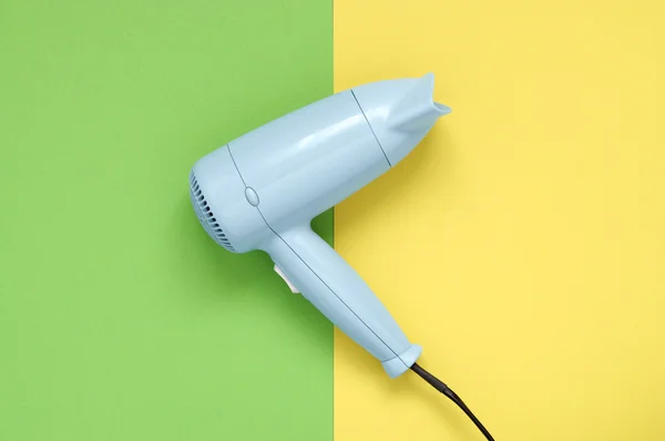 Blue hair dryer on green and yellow background — Stock Photo, Image