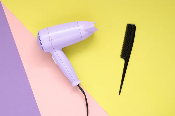 Secador de cabelo e pente sobre fundo de papel colorido — Fotografia de Stock