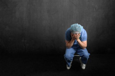 Bitkin, üzgün bir doktor karanlık bir odada oturuyor.