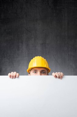 İnşaat işçisi elinde beyaz bir tahta tutuyor.