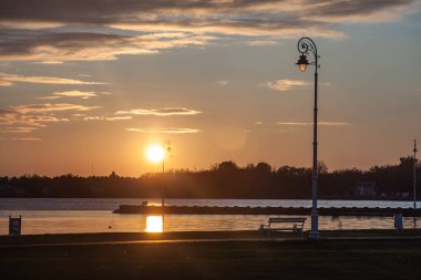 Sırbistan 'ın Subotica kentindeki Palic Gölü' nün önündeki halka açık bank ve sokak lambası, gün batımında önlerinde yeşil bir çim bulunuyor. Voyvodina 'nın büyük doğal bir simgesidir.