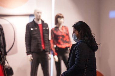 BELGRAD, SERBIA - 20 Ekim 2020: Orta yaşlı kadın, Coronavirus Covid 19 sağlık krizi sırasında bir giyim mağazasından mankenlerin önünde solunum maskesi takarak yürüyor