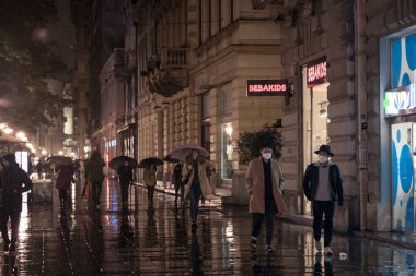 BELGRAD, SERBIA - 12 Ekim 2020: Gençler, iki Asyalı genç adam, arkadaşlar, yağmurlu bir gecede Coronavirus Covid 19 krizinde maske takarak yürüyorlar.