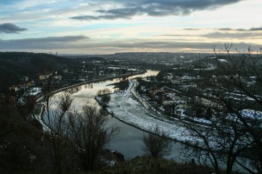 Panorama of prague seen from above from the Zamky hill, with a focus on the Moldau Vltava river and the settlement of Sedlec in winter, at dusk, in Czech republic