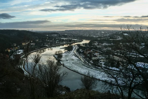 Panorama of prague seen from above from the Zamky hill, with a focus on the Moldau Vltava river and the settlement of Sedlec in winter, at dusk, in Czech republic