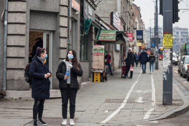 BELGRAD, SERBIA - 20 Şubat 2021: Kışın Belgrad sokaklarında Coronavirus covid 19 krizi üzerinde solunum maskesi takarak yürüyen iki kız, genç kadın ve arkadaş seçici bulanıklık