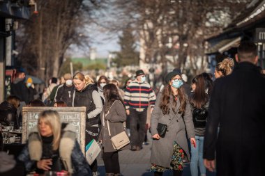 BELGRAD, SERBIA - 21 Şubat 2021: Kalabalık bir sokakta yüz maskesi takan ve Zemun 'daki kafelerde Coronavirus covid 19 krizi yaşayan genç bir kadın için seçici bulanıklık