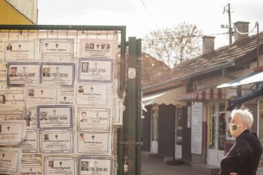 MLADENOVAC, SERBIA - 30 Nisan 2021: Coronavirus Covid 19 sağlık krizi sırasında maske takan ve ölüm ilanlarını okuyan yaşlı kadın