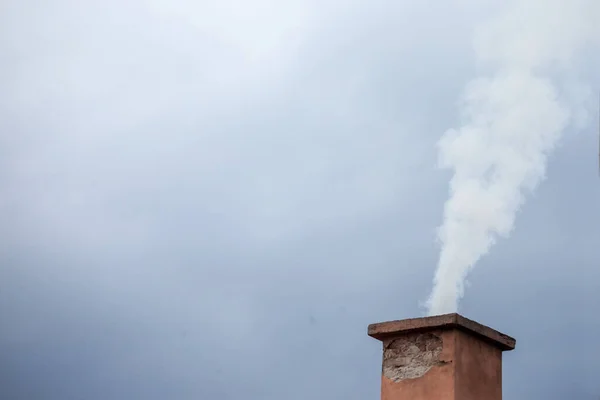 Selective blur on a smoking chimney rejecting white fume brick on the roof of an individual residential house exhausting little fumes at dusk, during a cloudy afternoon