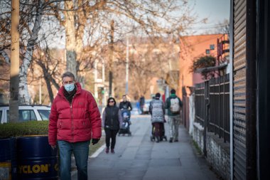 BELGRAD, SERBIA - 13 Şubat 2021: Coronavirus Covid 19 krizinde maske takan orta yaşlı adamlar Belgrad sokaklarında yürüyorlar