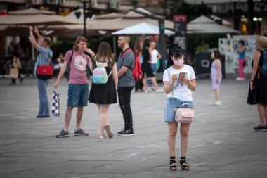 BELGRAD, SERBIA - 22 Haziran 2021: Koronavirüs kovid 19 sağlık krizi sırasında Belgrad caddesinde akıllı telefonundaki uygulamaları kontrol eden solunum maskesi takan Çinli, turist genç Asyalı kadın