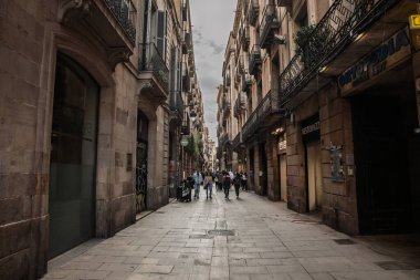 BARCELONA, İspanya - 5 Nisan 2025: Ciutat Vella 'da dar yaya sokağı, barri gotik Barcelona, cephelerle dolu. İnsanlar, Barselona 'nın eski kasabasını hissederek tarihi geçitte yürüyorlar..