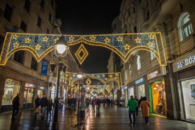 BELGRAD, SERBIA - 14 ARALIK 2024: Belgrad 'daki Kneza Mihailova yaya yolu geceleri noel ışıklarıyla süsleniyor. Noel ve Yeni Yıl atmosferini gösteren müşteriler