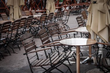 Slovenya 'nın Ljubljana kentindeki kapalı bir kafede boş ahşap sandalyeler ve yuvarlak masalar, katlanmış şemsiyeler ve ıslak kaldırımlar sezon dışı veya kapalı olduğunu gösteriyor..