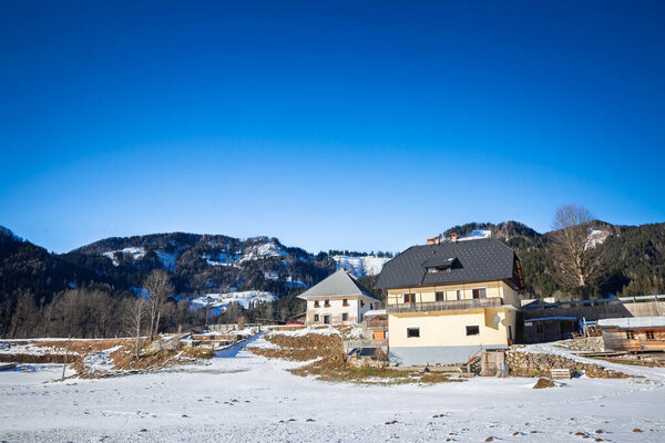 Шале в Юлианских Альпах, Словения. Солнечные дома стоят рядом с заснеженными метеорными столбами с вытянутыми шипами за ними, предлагая горную жизнь, вторые дома, возможности для недвижимости в живописной обстановке.