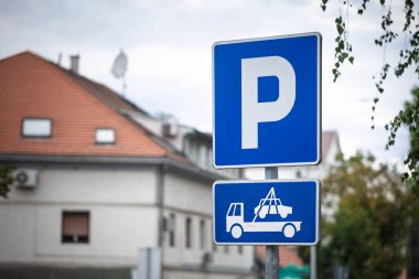 Sırbistan 'ın Belgrad kentindeki bir otoparkı işaret eden mavi Avrupa Otopark yol tabelasına yakından bakınca, fazladan bir plakada ihlallere karşı uyarıda bulunan bir çekici kamyonu görülüyor.