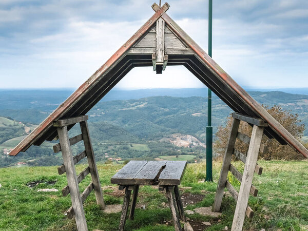 Простой деревянный приют для пикника с Афрамной крышей на Вр Раджаце, Сербия, рядом с видом на слоистые холмы. Раяц - это гора Сумадия в Динарических Альпах, сербское природное туристическое направление.
