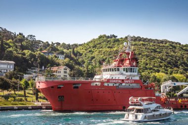 Kiyi Emniyeti 'nin kırmızı kıyı güvenlik gemisi, Türkçe Sahil Güvenlik, Boğaz kıyısında, yeşil tepeler ve deniz kıyısında evleri var. Gemi Türkiye 'nin deniz güvenliği ve kurtarma operasyonlarını temsil ediyor.