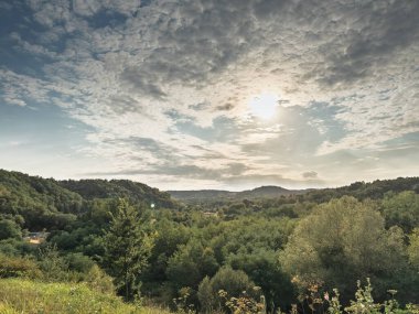Sırbistan 'ın orta kesimindeki Sumadija tepelerinin geniş manzarası. Güneş ışığı, ormanlar, çayırlar ve vadilerden oluşan bir mozaik üzerinde bölgenin yeşil kırsal alanını gösteren bulutları delip geçiyor..