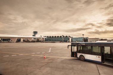 Bükreş Henri Coanda Otopeni Havaalanı Panoraması, Romanya 'nın ana havaalanındaki havaalanı operasyonlarını yakalayan terminal, kontrol kulesi ve geniş pistli park halindeki bir uçağın yanında bir önlük otobüsü gösteriyor..