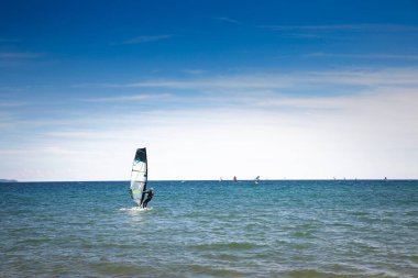LA LONDE, FRANCE - 27 SEPTEMBER 2025: Akdeniz 'de Fransız Rivierası' ndaki La Londe les Maures sahilinde rüzgar sörfü yapan bir adam, geniş mavi bir gökyüzü altında küçük dalgaların üzerinde süzülüyordu..