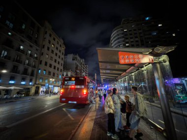 VALENCIA, İspanya - 9 Nisan 2025: Bir grup genç gece bir EMT Valencia otobüsü için otobüs durağında bekliyor. EMT ya da Empresa Belediye de Transportes de Valencia 'nın ulaşım yetkilisidir..