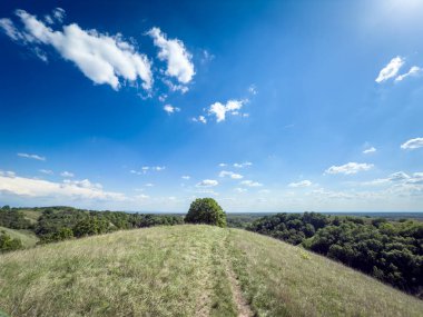Voyvodina 'daki Zagajicka brda' daki çimenli tepelerin geniş manzarası. Yuvarlanan Loess tepeleri ve soluk bir patika bu kendine özgü manzara boyunca parlak bir gökyüzü altında ormanlara doğru uzanır..