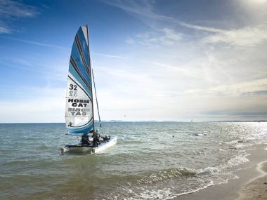 LA LONDE, FRANCE 27 EYLÜL 2025 Akdeniz kıyısında bir Hobie Cat katamaranı denize açılıyor. Çizgili yelkenli teknenin mürettebatı kıyı açıklarındaki sığ sularda..