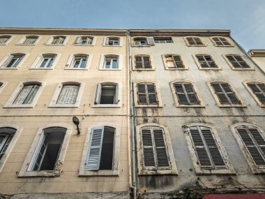 Güney Fransa, Toulon 'daki yaşlanan yerleşim alanının düşük açılı görüntüsü yıpranmış alçı, lekeli duvarlar ve eski panjurları gösteriyor. Binanın dış kısmı kentsel bozulmayı ve yenilenme ihtiyacını gösteriyor..