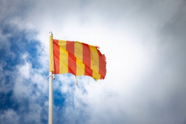 Güney Fransa 'da bulutlu mavi gökyüzüne karşı kırmızı ve sarı çizgili provenkal bayrak dalgaları, rüzgarlı hava, bölgesel kimliği, kültürü ve Provence mirasını sembolize ediyor..