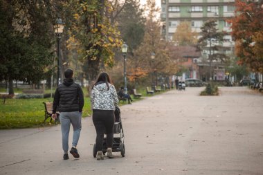 SUBOTICA, SERBIA - 9 Kasım 2025: Genç ebeveynler, Sırbistan 'ın Subotica kentinde günlük aile hayatı, ebeveynlik, Sırp toplumu ve nüfus grafikleri hakkında bir bebek arabasını park yolunda ittiler.