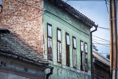 Sırbistan 'ın Belgrad kentindeki eski bir binanın çürüyen cephesine yakından bakınca, yeşil boya, açık tuğla, çatlak alçı, aşınmış ahşap pencereler, çatı kiremitleri ve kentsel çürüme görülüyor.