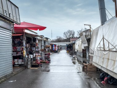 SUBOTICA, SERBIA - JANUARY 3, 2026: Empty lane inside Suboticki buvljak flea market in Subotica, Serbia, with closed metal stalls and merchandise under tarps after rain, wet pavement and puddles.