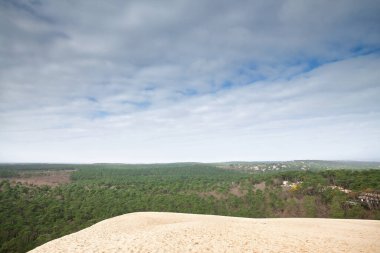 Pilat Dune 'un (Dune du Pyla) kumlu tepeleri ve yamaçları Arcachon Körfezi yakınlarındaki çam ormanlarına tepeden bakıyor, Aquitaine, Fransa, geniş bulutlu bir gökyüzü altında mavi benekli..