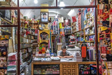 YAZD, IRAN - 18 AĞUSTOS 2016: Dükkan sahibi, Yazd, İran 'daki dolu bir okul ve ofis gereçleri mağazasında defter, ciltler, kalemler ve kırtasiye malzemeleriyle tezgahın arkasında oturuyor.