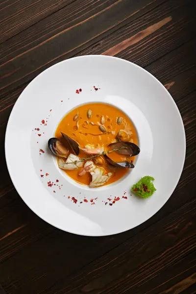 Creamy pumpkin soup with seafood, mussels, shrimps, squids, in a white plate, on a wooden background — Stock Image Creamy Pumpkin Soup Seafood Mussels Shrimps Squids White Plate Wooden Stock Picture