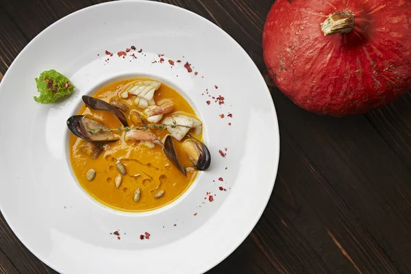 Creamy pumpkin soup with seafood, mussels, shrimps, squids, in a white plate, on a wooden background — Stock Image Creamy Pumpkin Soup Seafood Mussels Shrimps Squids White Plate Wooden Royalty Free Stock Images