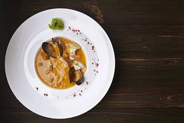 Creamy pumpkin soup with seafood, mussels, shrimps, squids, in a white plate, on a wooden background — Stock Image Creamy Pumpkin Soup Seafood Mussels Shrimps Squids White Plate Wooden Stock Picture