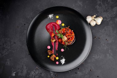 Siyah arka planda salata, sarımsaklı siyah bir tabakta.