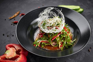 Sebze salatası, roka, dolma biber, salatalık ve keten tohumu, siyah arka planda.