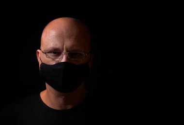 Ciddi, orta yaşlı, gözlüklü, siyah bir sağlık maskesi takmış, yüzünde siyah bir arkaplanda, mesaj atabileceği bir yer var.