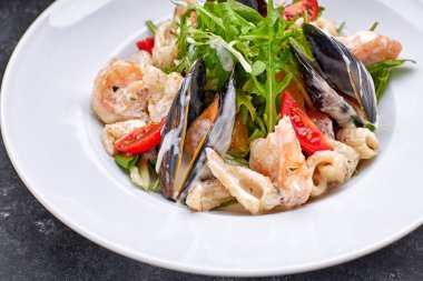 Kabuklu deniz ürünleri salatası, mürekkep balığı, karides, yuvarlak beyaz bir tabakta, gri bir arka planda.