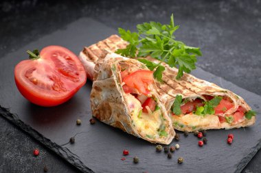 Shawarma kesme soslu, domatesli, peynirli, otlu ve sarımsaklı, siyah bir zemin üzerinde,