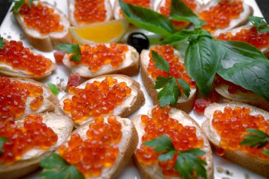 Beyaz tabakta kırmızı somon havyarlı sandviçler, yakın plan, sığ alan derinliği. Ziyafet dekorasyonu, yemek servisi.