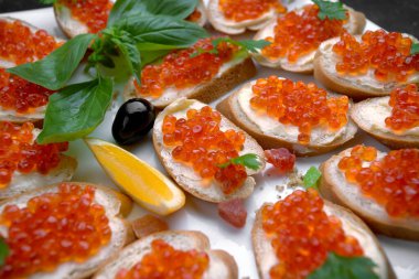 Beyaz tabakta kırmızı somon havyarlı sandviçler, yakın plan, sığ alan derinliği. Ziyafet dekorasyonu, yemek servisi.