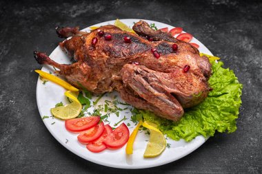 Kızarmış Noel ördeği, beyaz bir tabakta sebzelerle, koyu bir arka planda.