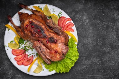 Kızarmış Noel ördeği, beyaz bir tabakta sebzelerle, koyu bir arka planda.