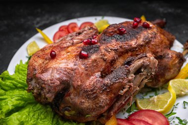 Kızarmış Noel ördeği, beyaz bir tabakta sebzelerle, koyu bir arka planda.